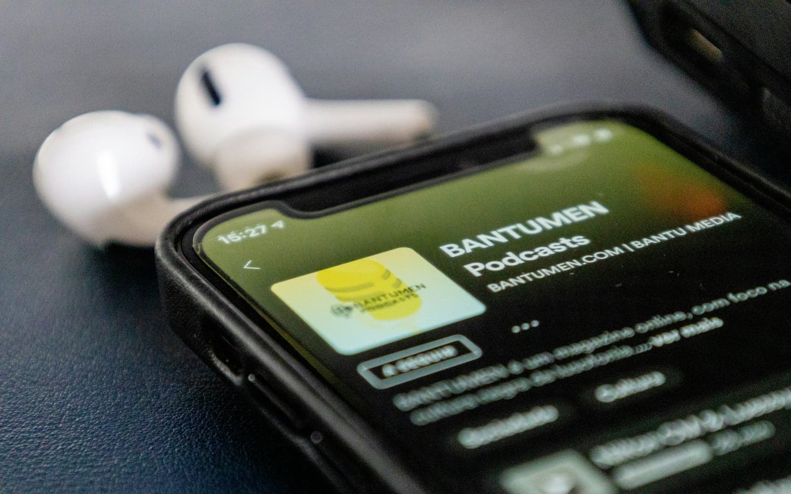 Smartphone met podcast-app en oortjes op een bureau